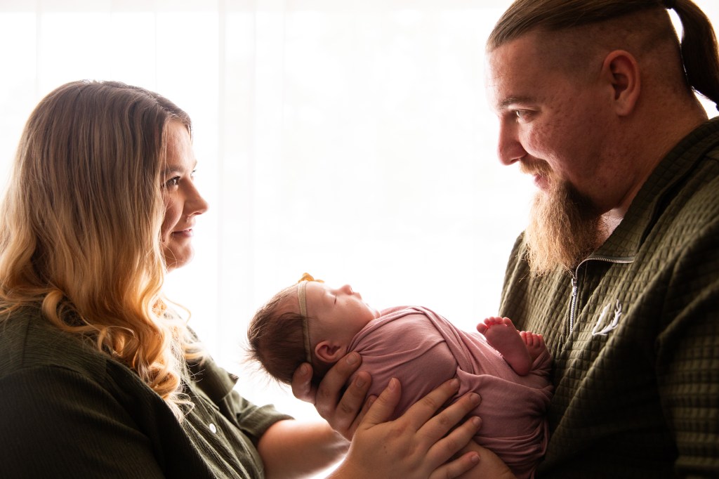 a blonde woman and a brown haired man with a beard holding a young baby
